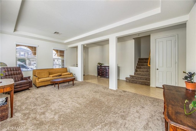 carpeted living area with tile patterned floors, stairway, visible vents, and a tray ceiling