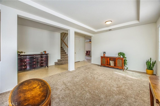 living area with visible vents, carpet flooring, tile patterned flooring, a raised ceiling, and stairs