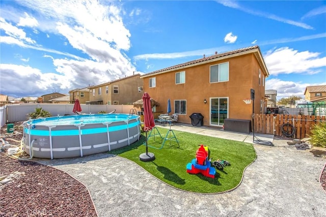 rear view of house featuring stucco siding, a fenced backyard, a yard, a fenced in pool, and a patio area