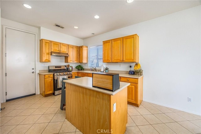 kitchen with visible vents, under cabinet range hood, light tile patterned flooring, stainless steel gas stove, and a sink