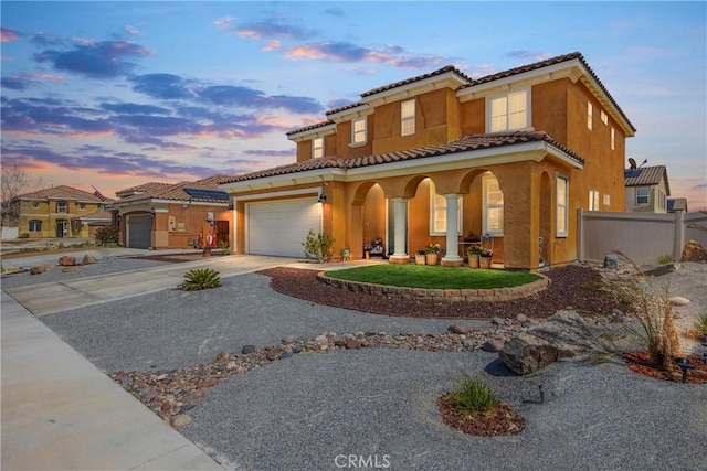 mediterranean / spanish-style home with stucco siding, driveway, a porch, fence, and a tiled roof