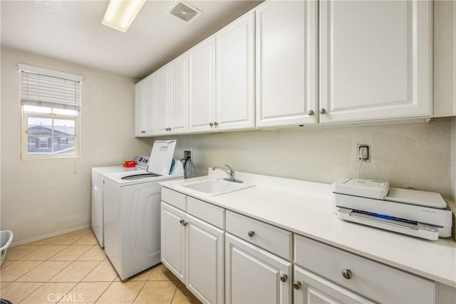 clothes washing area with washing machine and clothes dryer, visible vents, light tile patterned floors, cabinet space, and a sink