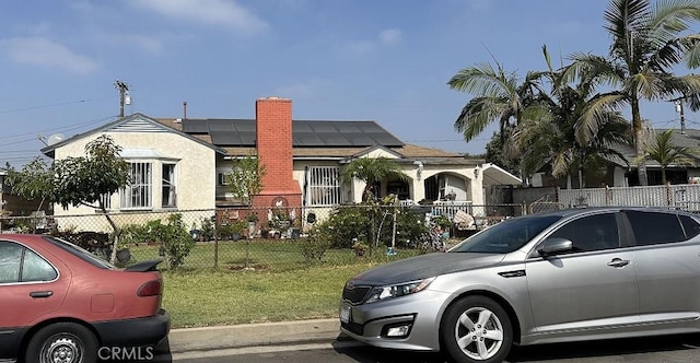 view of front of house featuring a fenced front yard, a front yard, a chimney, and solar panels