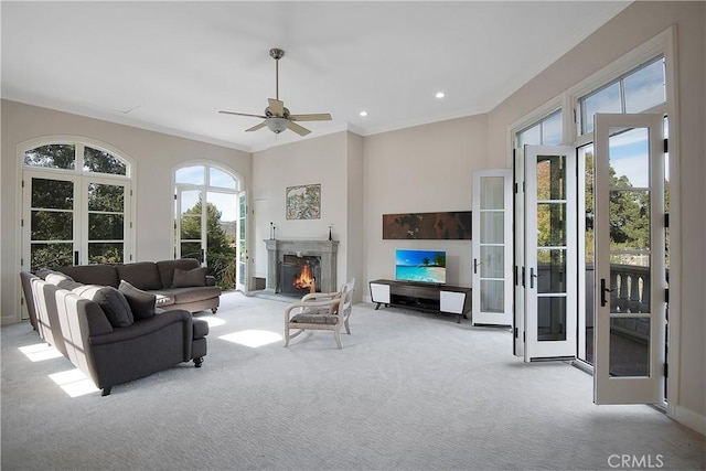 carpeted living room featuring recessed lighting, a warm lit fireplace, a healthy amount of sunlight, and crown molding