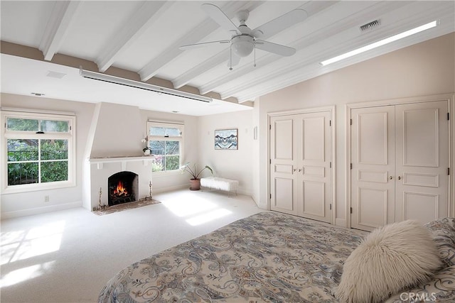 bedroom with lofted ceiling with beams, carpet floors, a fireplace, visible vents, and multiple closets