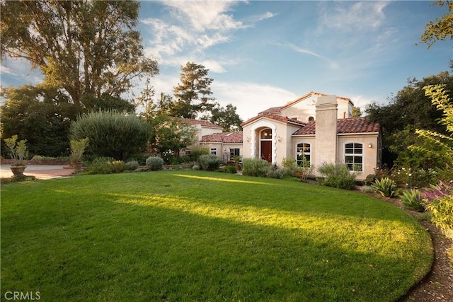 mediterranean / spanish-style house featuring a front yard, a tile roof, and stucco siding