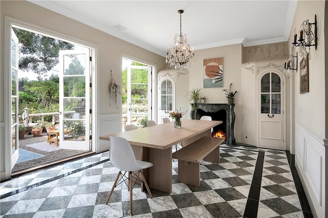 dining room with a chandelier, arched walkways, a premium fireplace, ornamental molding, and wainscoting