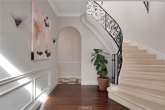 stairway featuring arched walkways, a decorative wall, wood finished floors, wainscoting, and crown molding