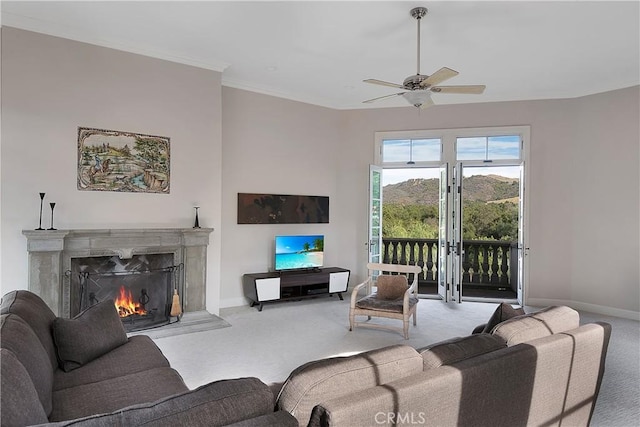 carpeted living room featuring ceiling fan, a fireplace with flush hearth, baseboards, french doors, and ornamental molding