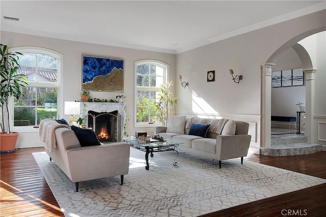 living room featuring visible vents, arched walkways, wood-type flooring, a lit fireplace, and crown molding