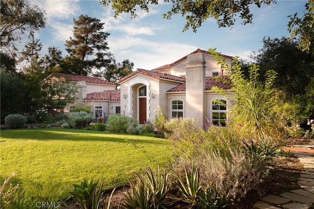 mediterranean / spanish home featuring a tiled roof, a front lawn, and stucco siding