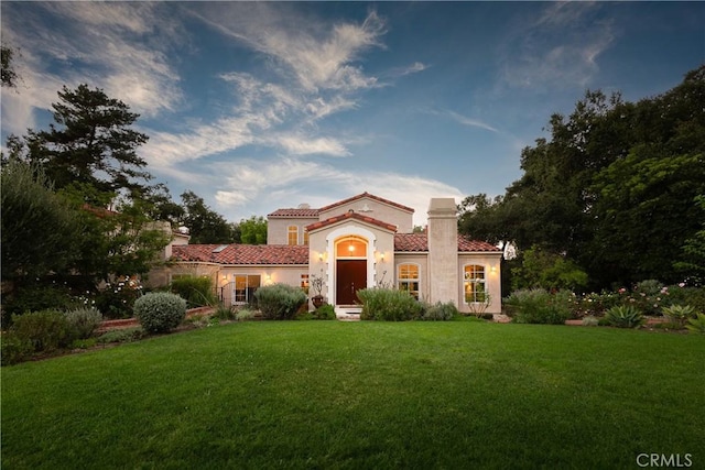 mediterranean / spanish house with stucco siding, a front yard, a chimney, and a tiled roof