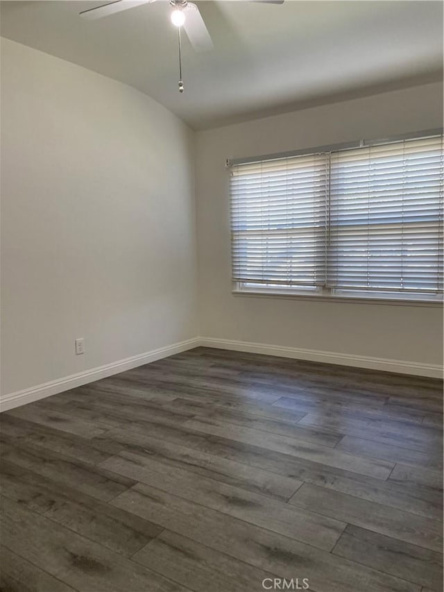 empty room featuring ceiling fan, baseboards, vaulted ceiling, and dark wood-style flooring