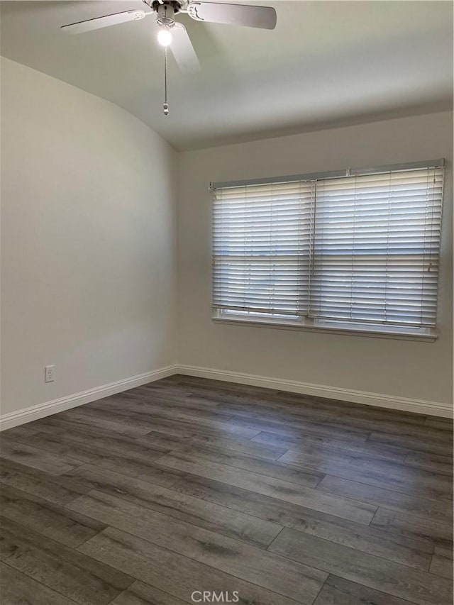 empty room with a ceiling fan, baseboards, vaulted ceiling, and dark wood-type flooring