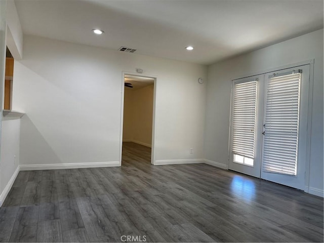 unfurnished room featuring dark wood-style flooring, visible vents, and baseboards