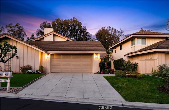 view of front of property with a yard, a chimney, concrete driveway, a garage, and a tiled roof