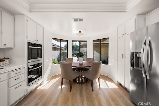 dining room featuring visible vents, baseboards, ornamental molding, and light wood finished floors