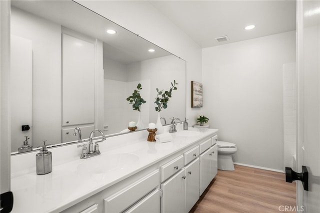 full bath featuring double vanity, toilet, wood finished floors, and a sink