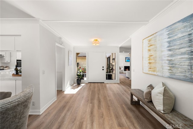 entryway with a lit fireplace, baseboards, crown molding, and light wood-style floors