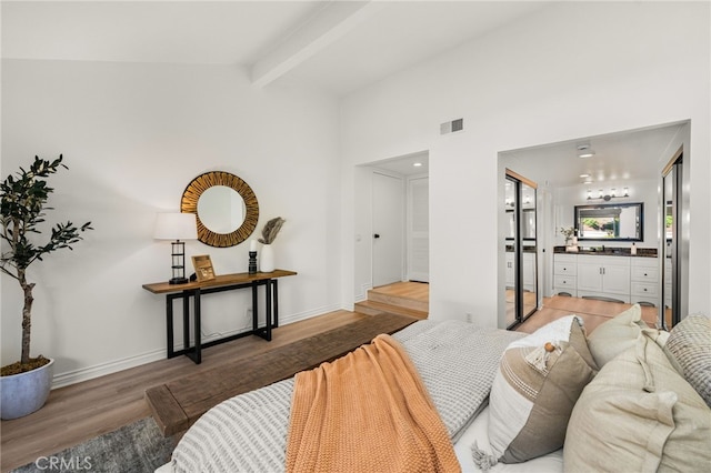 bedroom featuring visible vents, vaulted ceiling with beams, baseboards, light wood-style flooring, and ensuite bathroom