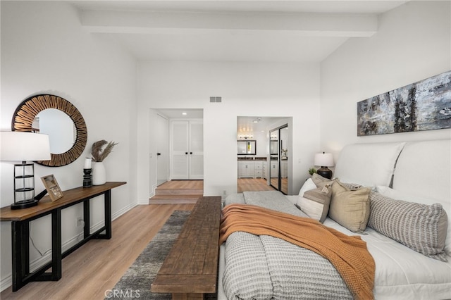 bedroom featuring visible vents, baseboards, light wood-style floors, and vaulted ceiling with beams