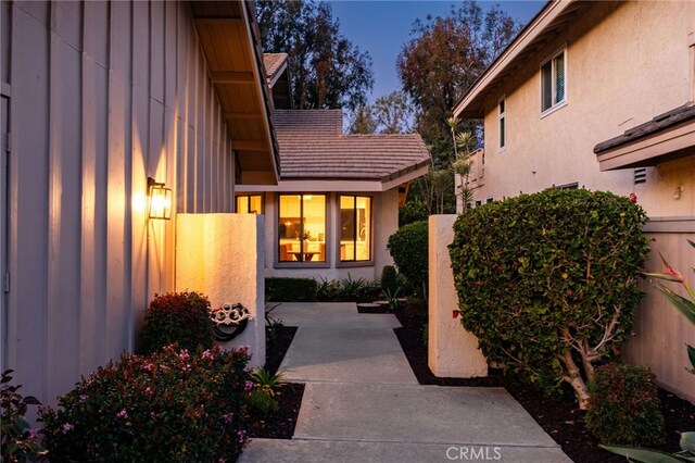 doorway to property featuring a tiled roof, fence, board and batten siding, and stucco siding