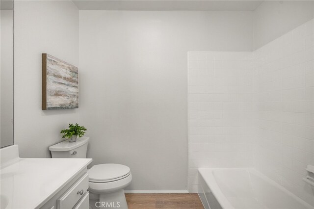 bathroom featuring baseboards, toilet, wood finished floors, and vanity