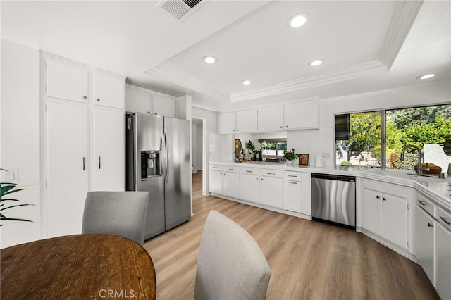 kitchen with visible vents, a tray ceiling, stainless steel appliances, light countertops, and light wood-style floors