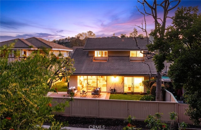 back of house at dusk with a tile roof and fence