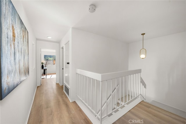 hallway with baseboards, an upstairs landing, visible vents, and wood finished floors