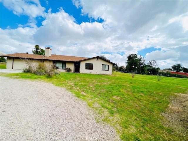 view of front of home featuring driveway, a front lawn, a chimney, and an attached garage