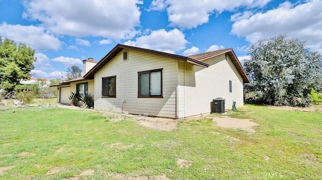 rear view of house featuring a garage, cooling unit, a yard, and a chimney