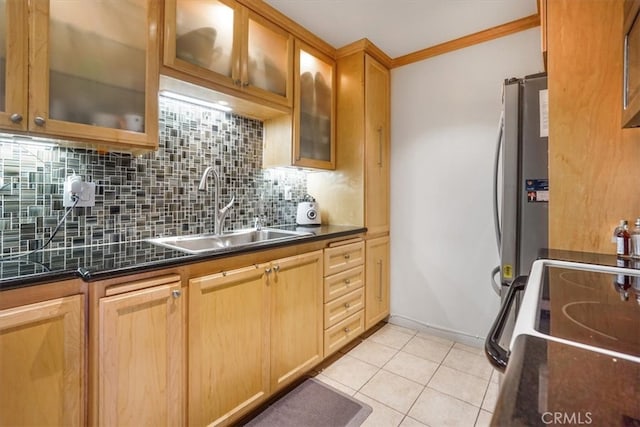 kitchen with light tile patterned floors, tasteful backsplash, dark countertops, freestanding refrigerator, and a sink