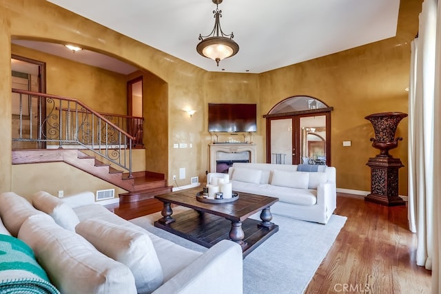 living room featuring arched walkways, a premium fireplace, wood finished floors, visible vents, and baseboards