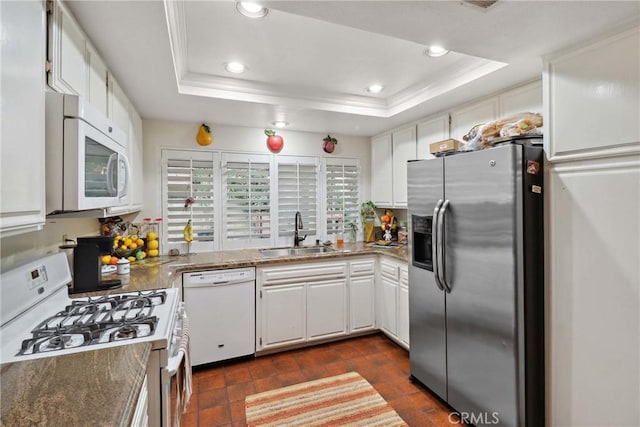 kitchen with a tray ceiling, white appliances, a sink, and white cabinetry