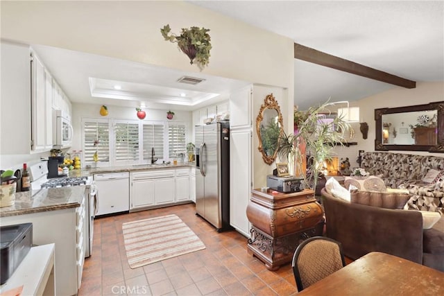 kitchen featuring a raised ceiling, visible vents, white cabinetry, a sink, and white appliances