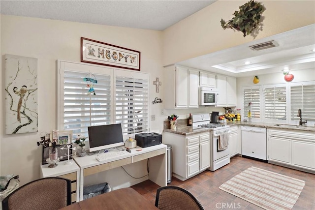 kitchen with white appliances, visible vents, a raised ceiling, white cabinetry, and a sink