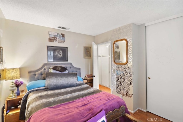 bedroom with a closet, visible vents, a textured ceiling, and wood finished floors