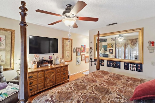 bedroom featuring ceiling fan, a textured ceiling, visible vents, and wood finished floors