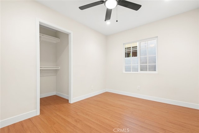 unfurnished bedroom featuring a closet, light wood-style flooring, a spacious closet, a ceiling fan, and baseboards