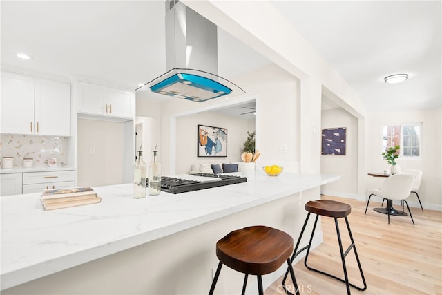 kitchen with light stone counters, a breakfast bar area, light wood-style flooring, white cabinetry, and island range hood