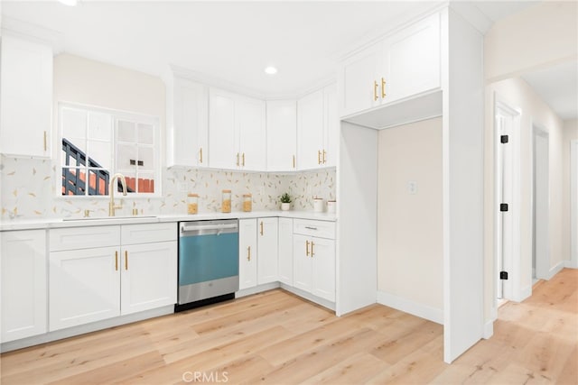 kitchen featuring tasteful backsplash, light countertops, stainless steel dishwasher, white cabinets, and a sink