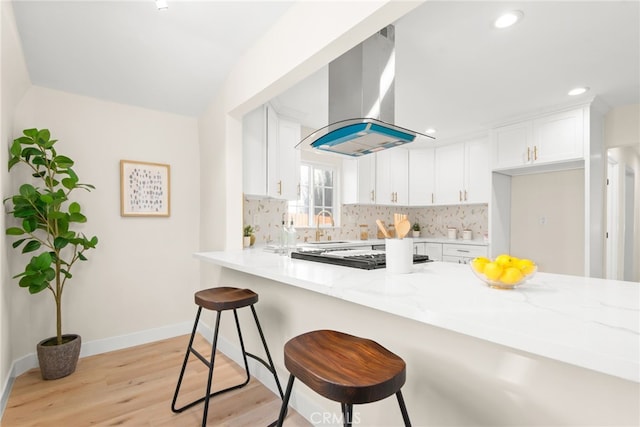 kitchen with tasteful backsplash, range hood, white cabinetry, and light stone countertops