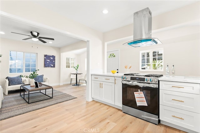 kitchen featuring light wood-style flooring, white cabinets, light countertops, stainless steel range with gas cooktop, and island exhaust hood