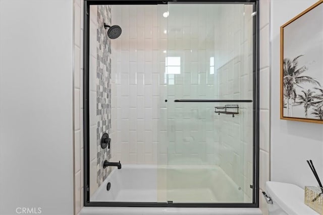 bathroom featuring toilet and bath / shower combo with glass door