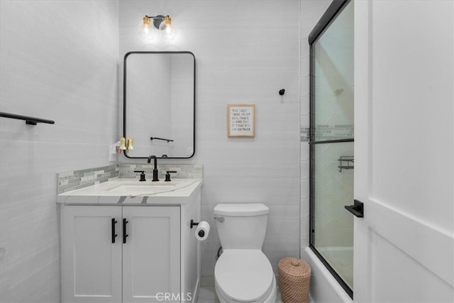 bathroom featuring toilet, vanity, tile walls, and bath / shower combo with glass door