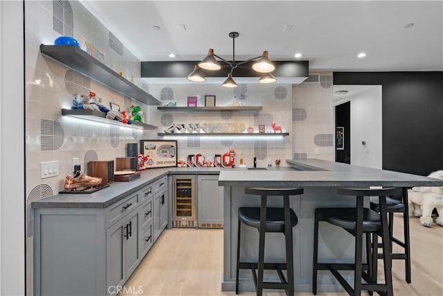 kitchen featuring beverage cooler, light wood finished floors, a breakfast bar, open shelves, and decorative backsplash