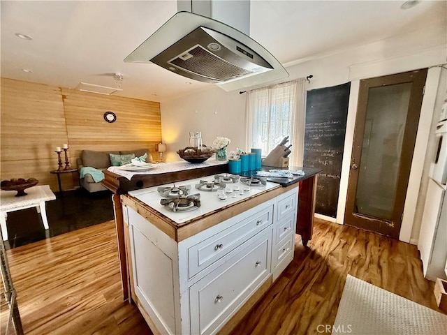 kitchen featuring wooden walls, wood finished floors, white gas cooktop, exhaust hood, and white cabinetry