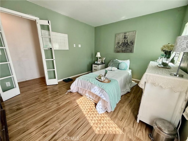 bedroom with french doors, wood finished floors, and baseboards