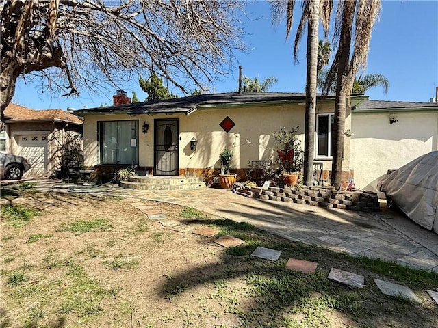 single story home featuring an attached garage, a chimney, and stucco siding